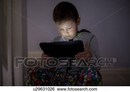 Stock Photograph - Boy using a digital tablet in the dark. Fotosearch