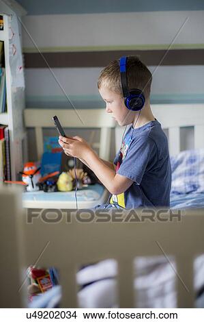 Picture - Boy wearing headphones using device. Fotosearch