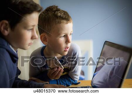 Boys using smartphone and laptop View Large Photo Image Stock Image - Boys using smartphone and laptop. Fotosearch