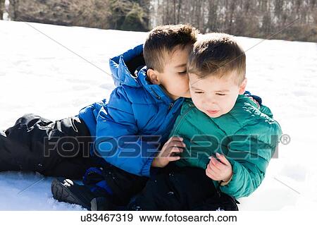 Stock Photo - Brother sitting on snow whispering to preschool boy. Fotosearch
