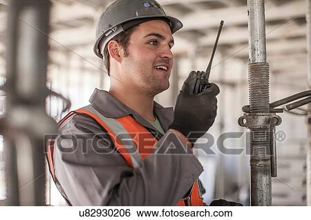 Builder using walkie talkie on construction site View Large Photo Image Stock Photograph - Builder using walkie talkie on construction site. Fotosearch
