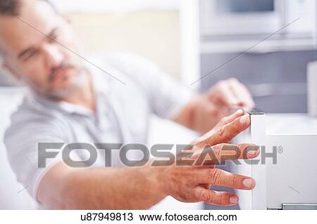 Stock Image - Close up of joiner installing drawers in kitchen. Fotosearch
