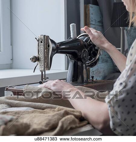 Stock Image - Close up of woman sewing textiles on vintage sewing machine. Fotosearch