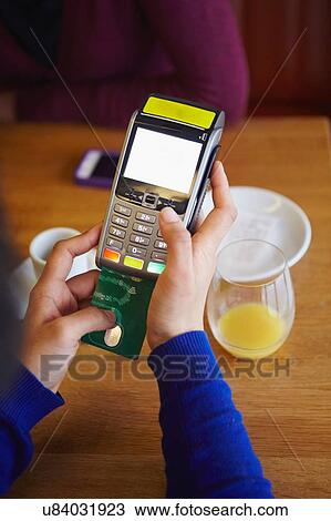 Stock Image - Close up of womans hands inserting card into credit card machine in restaurant. Fotosearch