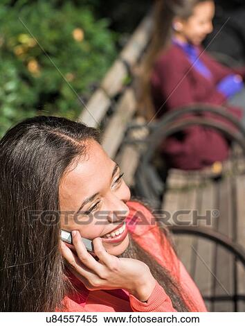 Close up of young woman sitting on park bench chatting on smartphone View Large Photo Image Stock Photography - Close up of young woman sitting on park bench chatting on smartphone. Fotosearch