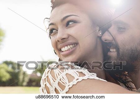 Stock Image - Close up portrait of young couple hugging looking away smiling. Fotosearch