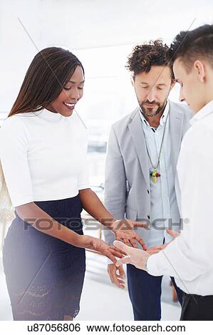 Stock Photograph - Colleagues in team building task face to face holding hands looking down smiling. Fotosearch