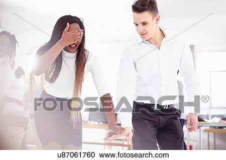 Stock Image - Colleagues in team building task, hand covering eyes, holding hands. Fotosearch