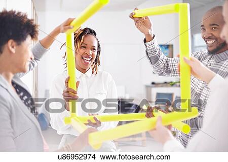 Picture - Colleagues in team building task holding yellow rubes smiling. Fotosearch