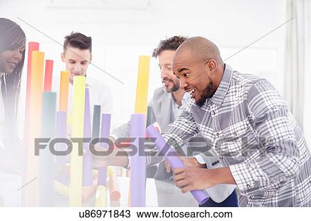 Stock Image - Colleagues in team building task balancing colourful tubes smiling. Fotosearch