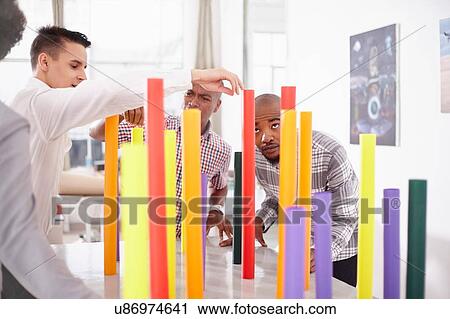 Stock Image - Colleagues in team building task balancing colourful tubes. Fotosearch