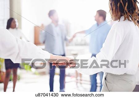 Stock Image - Colleagues in team building task standing in circle holding hands. Fotosearch