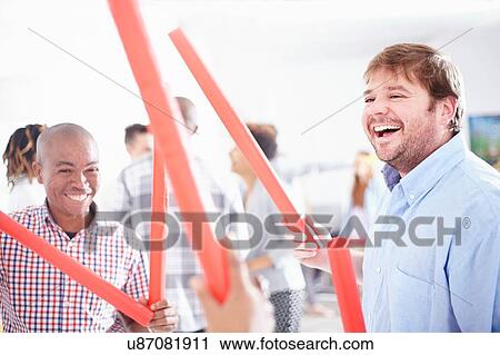 Stock Image - Colleagues in team building task, holding red tubes smiling. Fotosearch