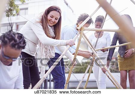 Stock Photography - Colleagues in team building task building wooden structure smiling. Fotosearch