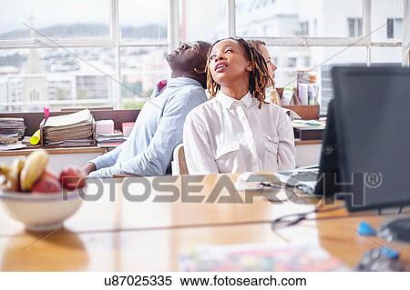 Stock Photography - Colleagues in team building task sitting back to back looking away. Fotosearch