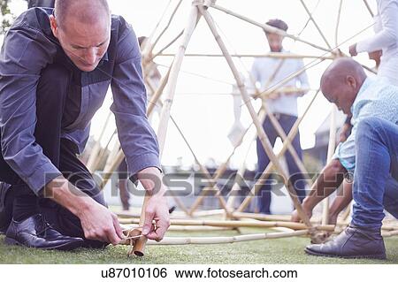 Stock Photograph - Colleagues kneeling down building wooden structure. Fotosearch