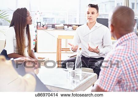 Picture - Colleagues sitting around coffee table chatting. Fotosearch