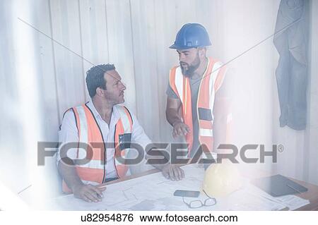 Stock Photograph - Construction foreman and builder meeting at desk in portable cabin. Fotosearch