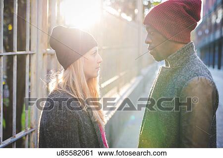 Stock Image - Couple face to face beside steel fence. Fotosearch