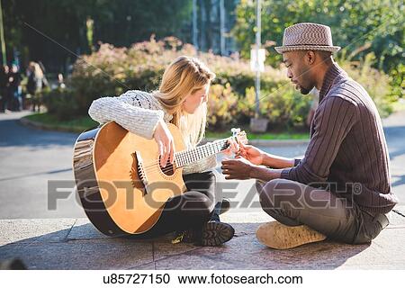 Stock Image - Couple learning to play guitar in park. Fotosearch