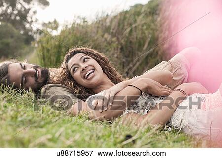 Stock Photo - Couple lying on grass hugging, smiling. Fotosearch