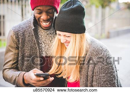 Picture - Couple smiling at message on smartphone. Fotosearch