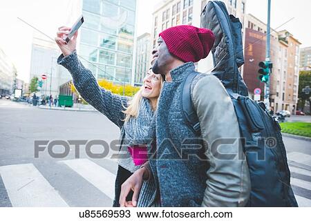 Stock Image - Couple taking selfie with smartphone on street. Fotosearch