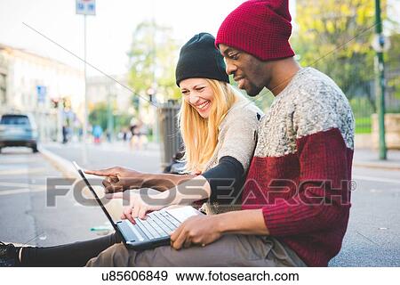 Couple using laptop on pavement View Large Photo Image Stock Photo - Couple using laptop on pavement. Fotosearch