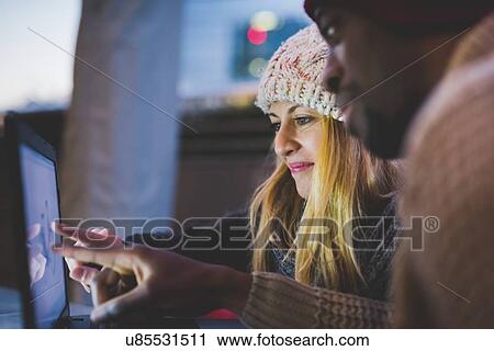 Stock Image - Couple using laptop outdoors at dusk. Fotosearch