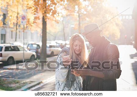 Stock Image - Couple using smartphone on pavement. Fotosearch