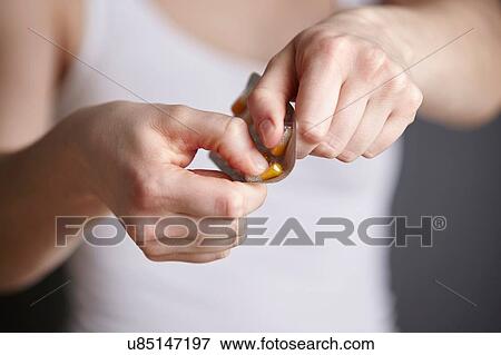 Stock Photo - Cropped close up of young woman removing medicine capsule from blister pack. Fotosearch