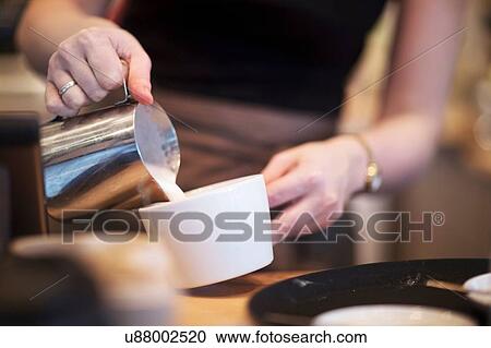 Stock Image - Cropped shot of waitress pouring milk into coffee cup in cafe. Fotosearch