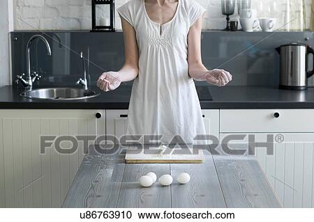 Stock Image - Cropped shot of woman baking with eggs and flour at kitchen table. Fotosearch