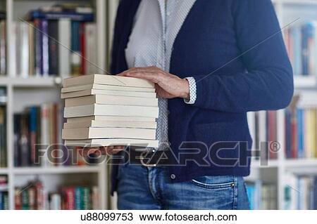 Stock Image - Cropped shot of woman carrying stack of books from bookshelves. Fotosearch