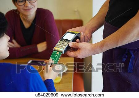 Stock Photo - Cropped shot of woman inserting card into credit card machine in restaurant. Fotosearch