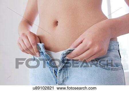 Stock Image - Cropped shot of young woman fastening jeans. Fotosearch