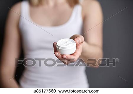 Stock Image - Cropped shot of young woman holding moisturiser jar. Fotosearch
