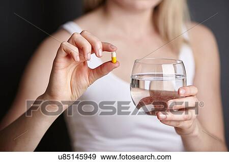 Cropped shot of young woman holding medicine capsule and glass of water View Large Photo Image Stock Photo - Cropped shot of young woman holding medicine capsule and glass of water. Fotosearch