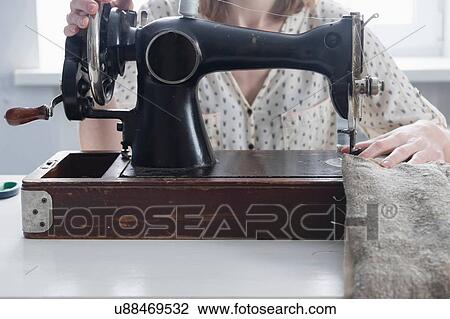Stock Image - Cropped view of mid adult woman sewing on vintage sewing machine. Fotosearch