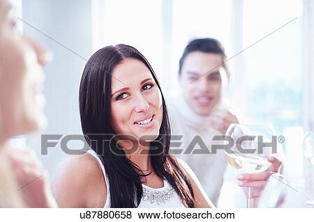 Stock Photo - Cropped view of three young adult friends chatting and drinking wine in kitchen. Fotosearch