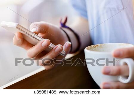 Cropped view of young womans hands holding coffee cup using smartphone View Large Photo Image Stock Photography - Cropped view of young womans hands holding coffee cup using smartphone. Fotosearch