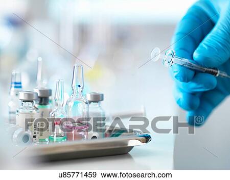 Stock Photo - Doctor placing syringe back onto tray with drug vials. Fotosearch