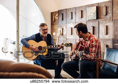 Picture - Father and adult son playing guitar in living room. Fotosearch