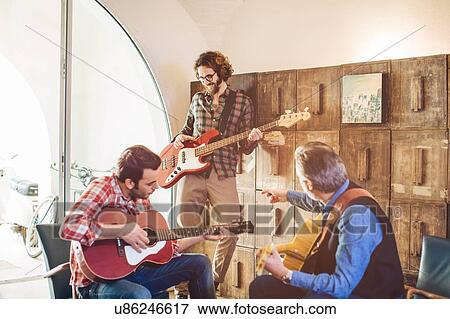 Stock Photo - Father and two adult sons having guitar practice in living room. Fotosearch