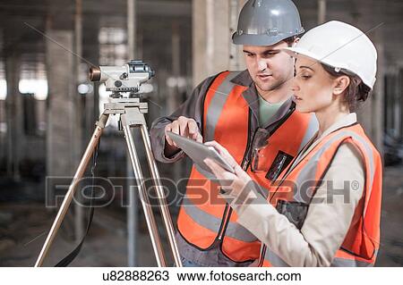 Stock Image - Female and male surveyor using digital tablet on construction site. Fotosearch