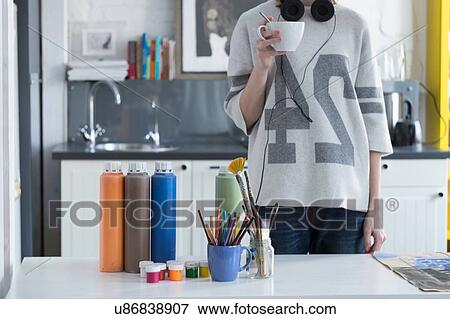 Stock Photo - Female artist drinking coffee at kitchen table. Fotosearch