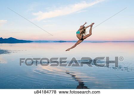 Stock Photo - "Female ballet dancer leaping mid air over lake, Bonneville Salt Flats, Utah, USA". Fotosearch