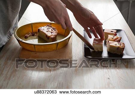 Stock Image - Female hands placing cake onto dish at kitchen counter. Fotosearch