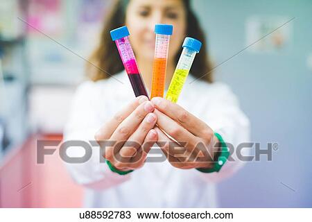 Stock Image - Female scientist holding solution of three different fluorescent dyes. Fotosearch