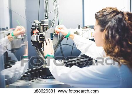 Stock Image - Female scientist positioning thin film sample on sample holder on x-ray diffractometer. Fotosearch